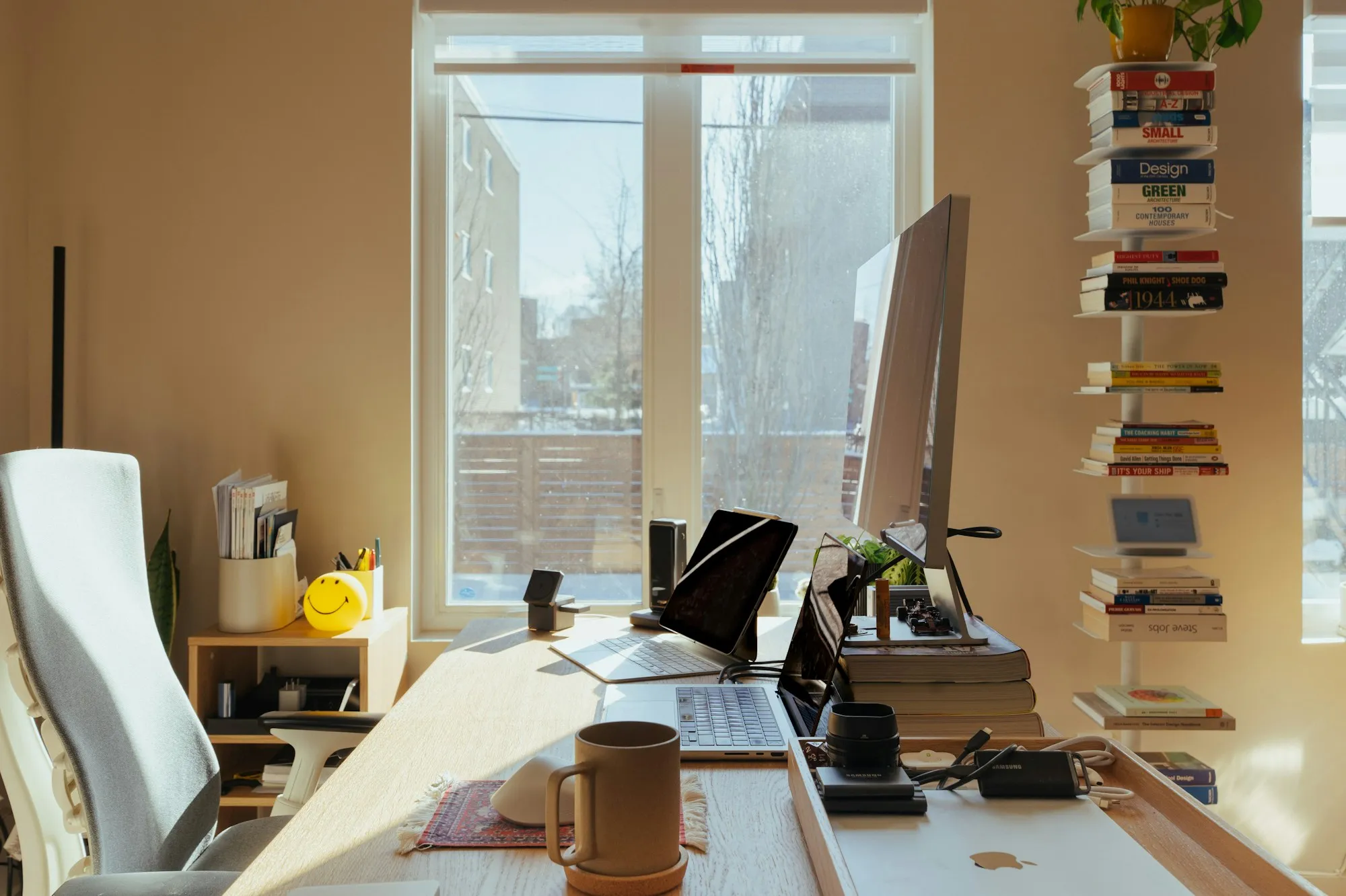 A sunlit office desk with a computer and shelves of books