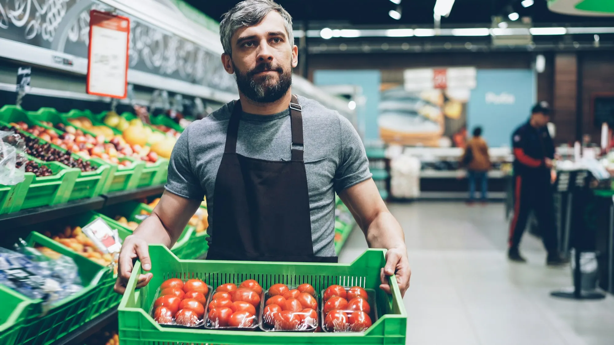 A grocery worker holding a crate of tomatoes in the produce section